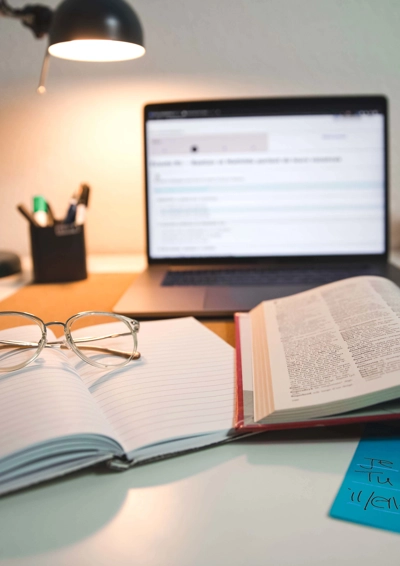 Ordbøger, notesbog og computerskærm med læsebriller